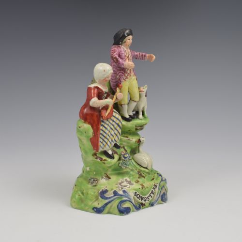 fig 1. An antique Staffordshire pearlware figure group titled Songsters depicting a seated woman playing an instrument alongside a standing man, a dog, and a swan on a green mound base.