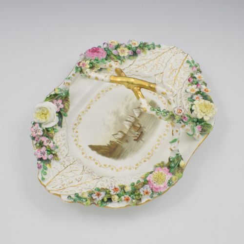 fig 2. A white porcelain basket decorated with hand-sculpted flowers along the rim, a gilded twig-shaped handle, and a hand-painted marine landscape scene in the centre.