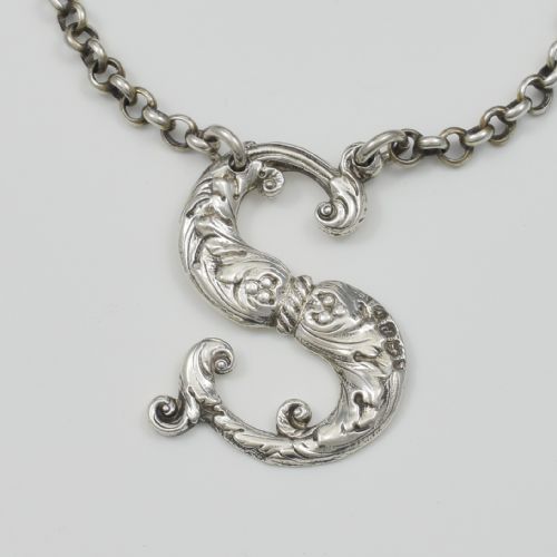 fig 1. An antique Georgian sterling silver decanter label shaped as the letter S with chased foliate scrollwork and an attached chain.