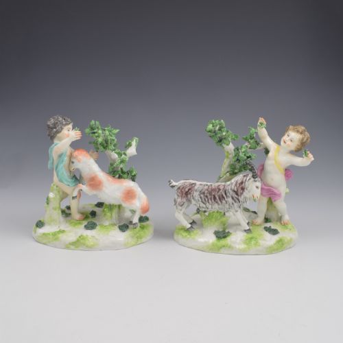 fig 1. A pair of hand-painted porcelain figures featuring young putti standing alongside goats amidst green leafy foliage on rounded naturalistic bases.