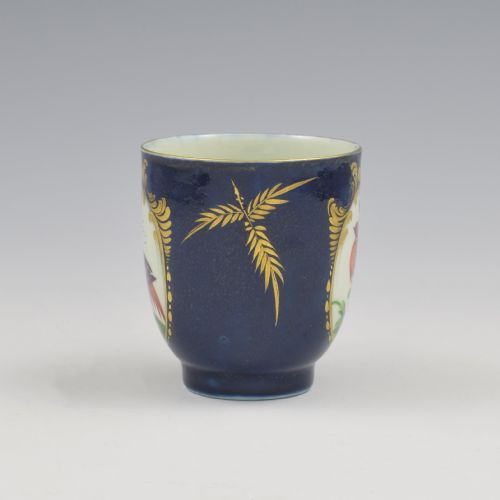 fig 1. A dark blue soft-paste porcelain coffee cup decorated with a gilded cartouche enclosing a painted exotic bird on a foliage branch.