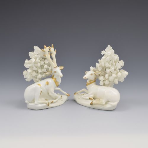fig 1. A pair of white glazed porcelain figures representing a recumbent stag and doe with gilded accents set against floral bocage tree backgrounds.