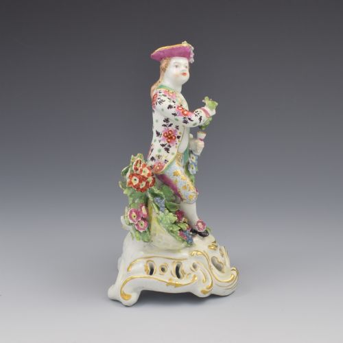 fig 1. An 18th-century Bow soft-paste porcelain figure depicting an allegorical youth standing beside floral bocage on a pierced gilded scroll base.