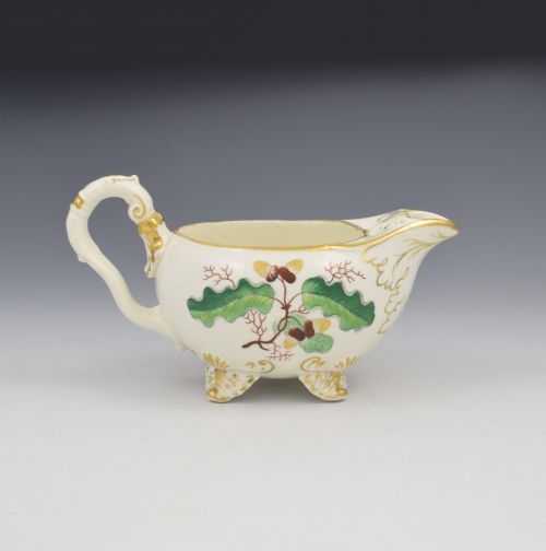 fig 1. A cream-coloured Regency porcelain jug featuring hand-painted green oak leaves, brown acorns, moulded feet, and gilded trim.