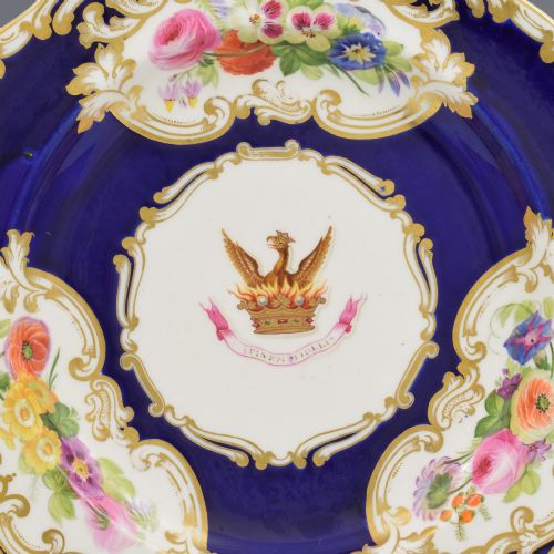 fig 2. A 19th-century Copeland porcelain plate featuring a cobalt blue border with gilt scrollwork, hand-painted floral cartouches, and a central heraldic crest depicting a phoenix in flames above a coronet.