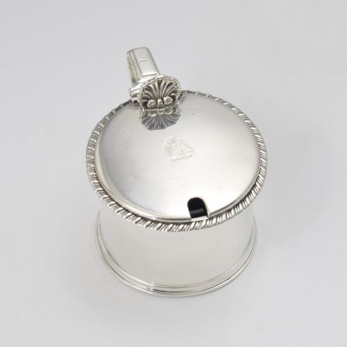 fig 1. A cylindrical Georgian sterling silver drum mustard pot featuring a hinged lid, shell thumbpiece, and engraved crest.