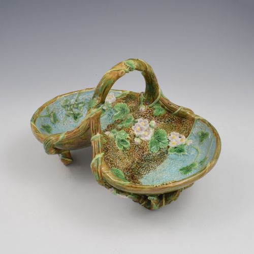 fig 1. A Victorian George Jones majolica strawberry basket featuring double compartments decorated with relief leaves, pink blossoms, and an overarching branch handle in green, brown, and turquoise glazes.