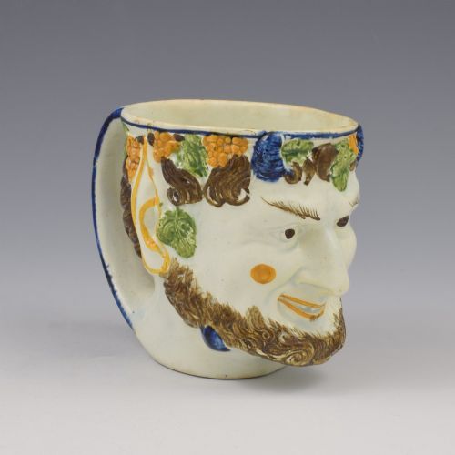 fig 1. A late 18th-century pearlware ceramic mug formed as a satyrs head with relief-moulded beard, pointed ears, and grapevines in underglaze colours.