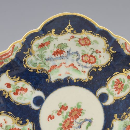 fig 1. A scalloped Dr Wall Worcester porcelain teapot stand featuring a hand-painted blue scale ground, gilded rococo cartouches, and colourful Kakiemon-style floral motifs.
