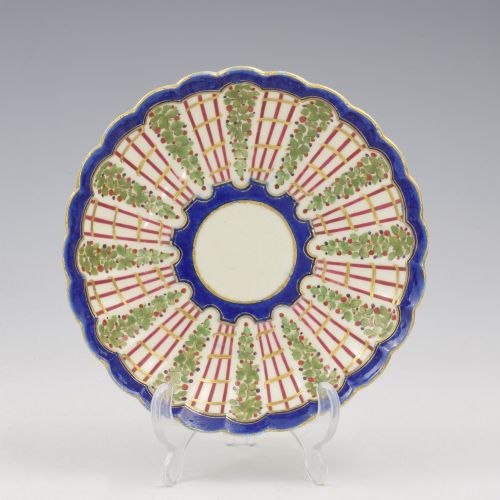 fig 1. An 18th-century soft-paste porcelain coffee cup and saucer with fluted edges, featuring a cobalt blue border, gilt highlights, and a painted green hop trellis pattern.
