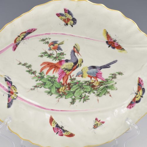fig 1. An eighteenth-century leaf-moulded soft-paste porcelain dish featuring central hand-painted fancy birds, surrounding butterflies, a pink stalk handle, and a gilded edge.