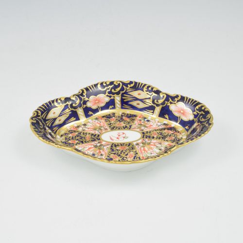 fig 1. An oval antique Royal Crown Derby porcelain serving dish featuring intricate cobalt blue, coral red, and heavy gold leaf Imari pattern 6299 details with a lobed edge.