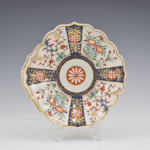 fig 1. An 18th-century circular soft-paste porcelain dish with a scalloped rim, decorated in the Rich Queens pattern featuring cobalt blue gilt panels alternating with painted red and green floral motifs.