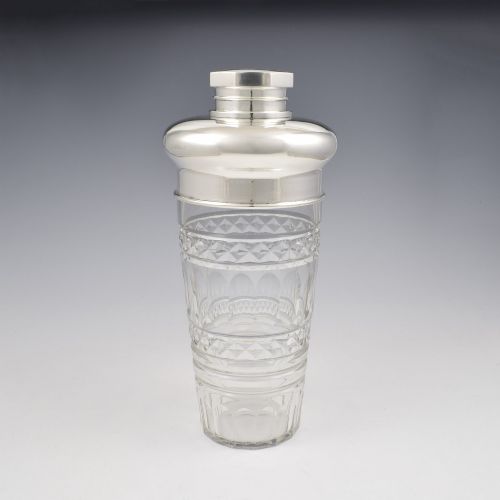 fig 1. An Art Deco cocktail shaker featuring a clear cut glass body with geometric facet patterns and a polished sterling silver mount and octagonal cap.