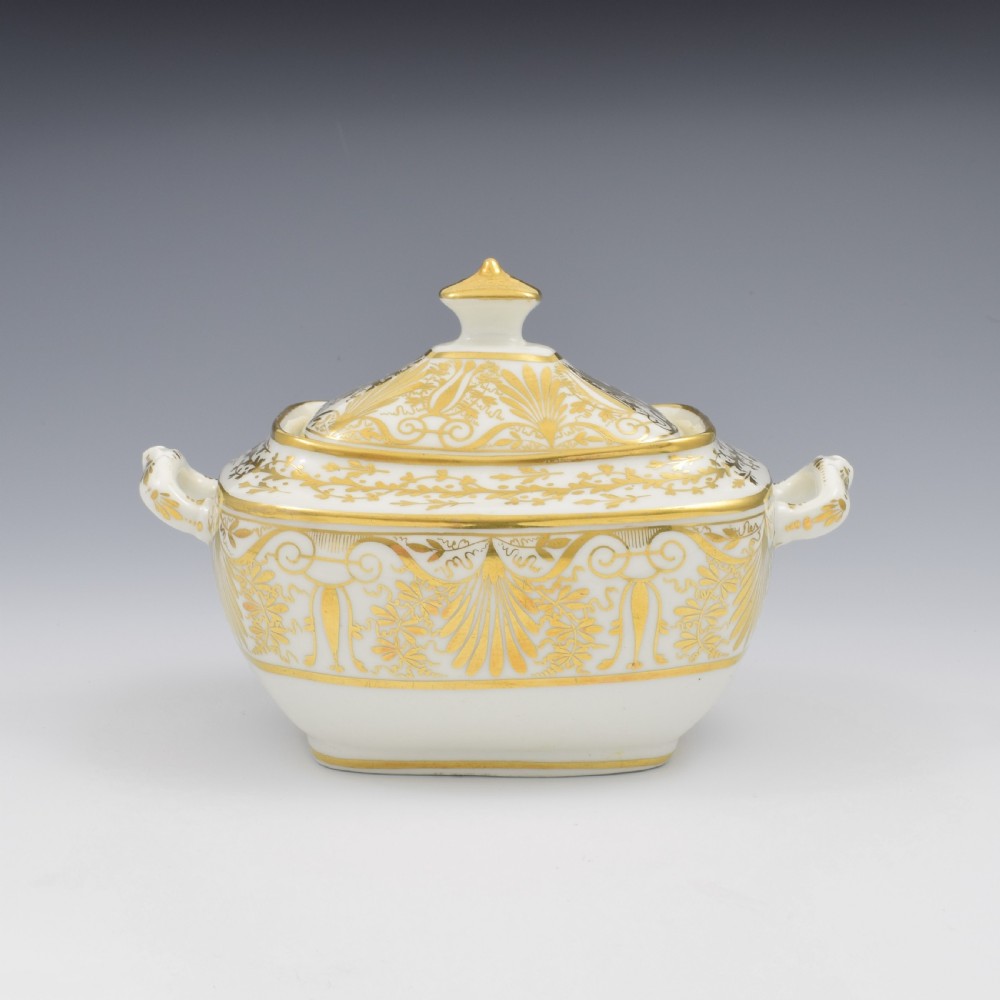 A white and gold Regency Spode porcelain sugar box with original lid, featuring loop handles and Neoclassical gilt scroll patterning.