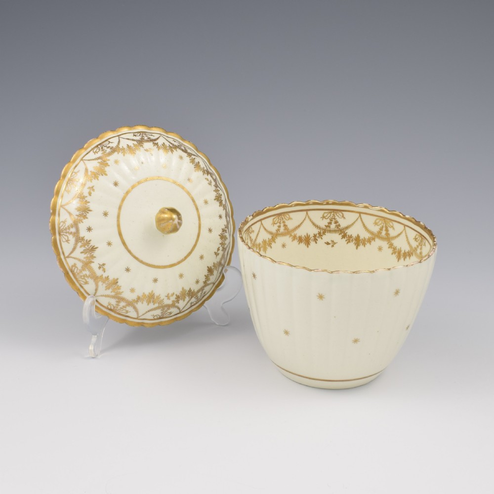 An eighteenth-century fluted cream porcelain sucrier and fitted cover adorned with gold gilded swags and star motifs.