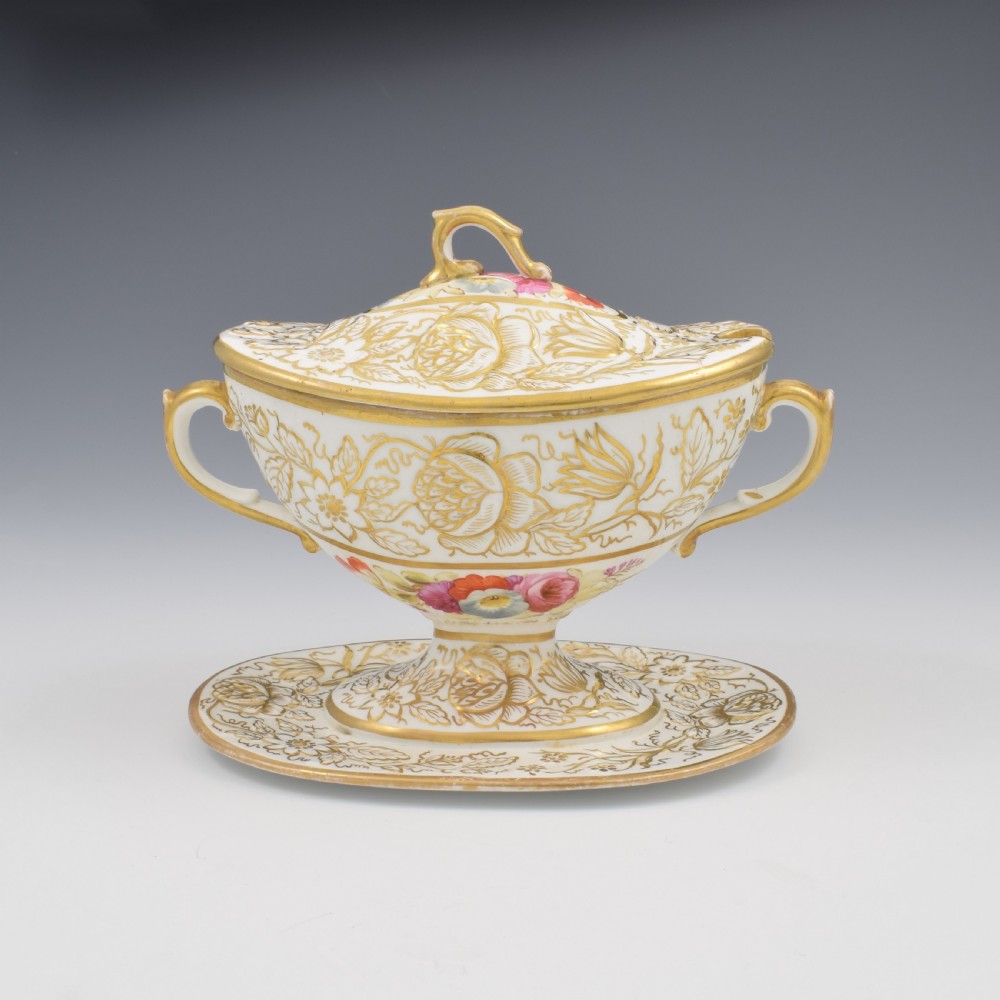A Regency era white porcelain sauce tureen featuring gilded floral designs, hand-painted botanical flowers, twin side handles, and a matching stand.
