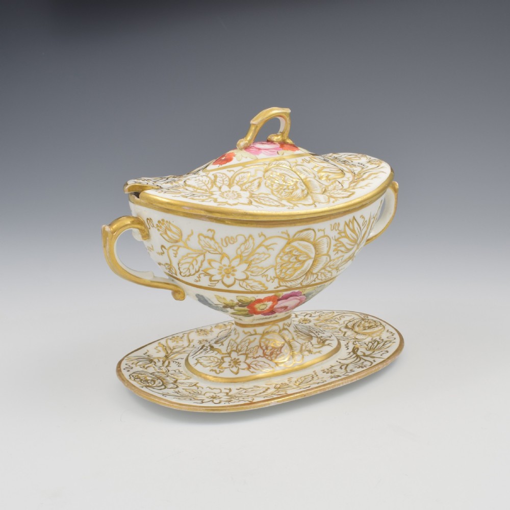 A Regency era white porcelain sauce tureen featuring gilded floral designs, hand-painted botanical flowers, twin side handles, and a matching stand. View VII