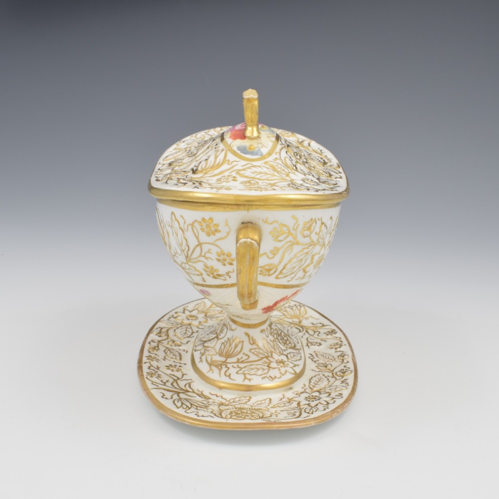A Regency era white porcelain sauce tureen featuring gilded floral designs, hand-painted botanical flowers, twin side handles, and a matching stand. View IX