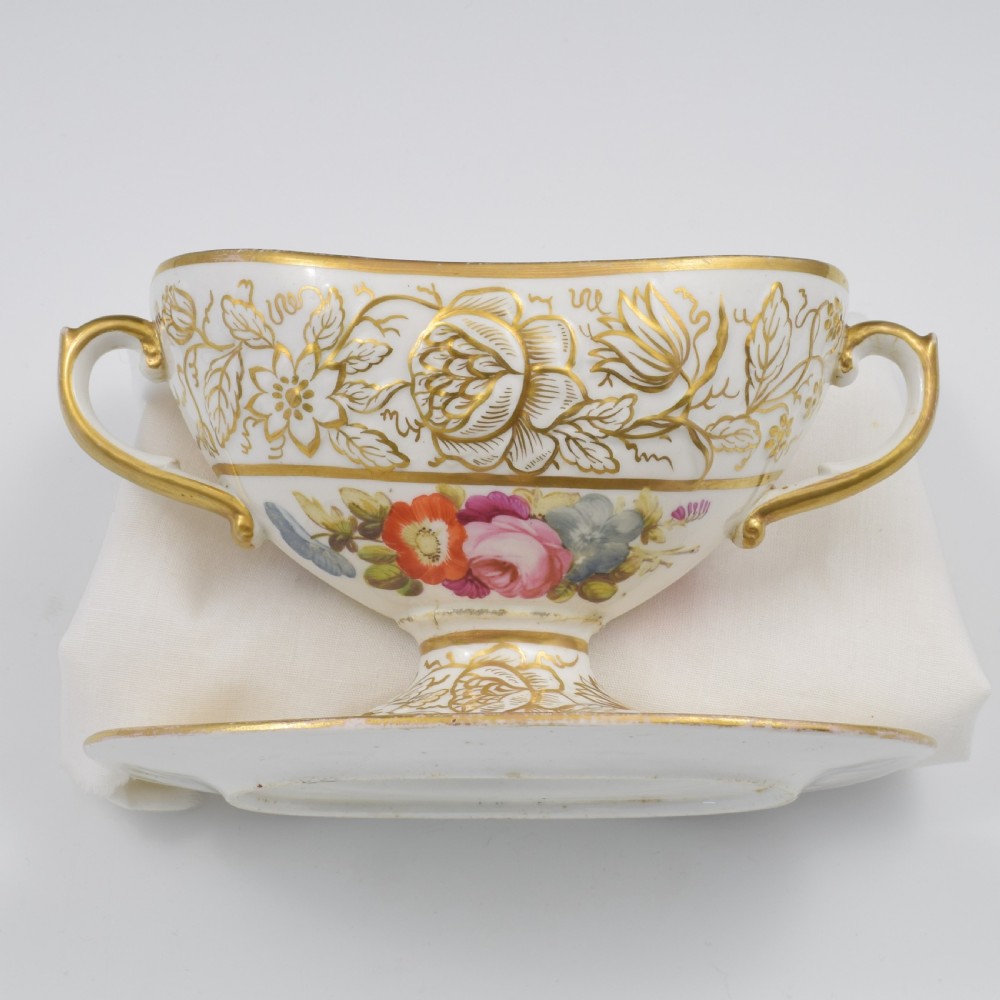 A Regency era white porcelain sauce tureen featuring gilded floral designs, hand-painted botanical flowers, twin side handles, and a matching stand. View XV