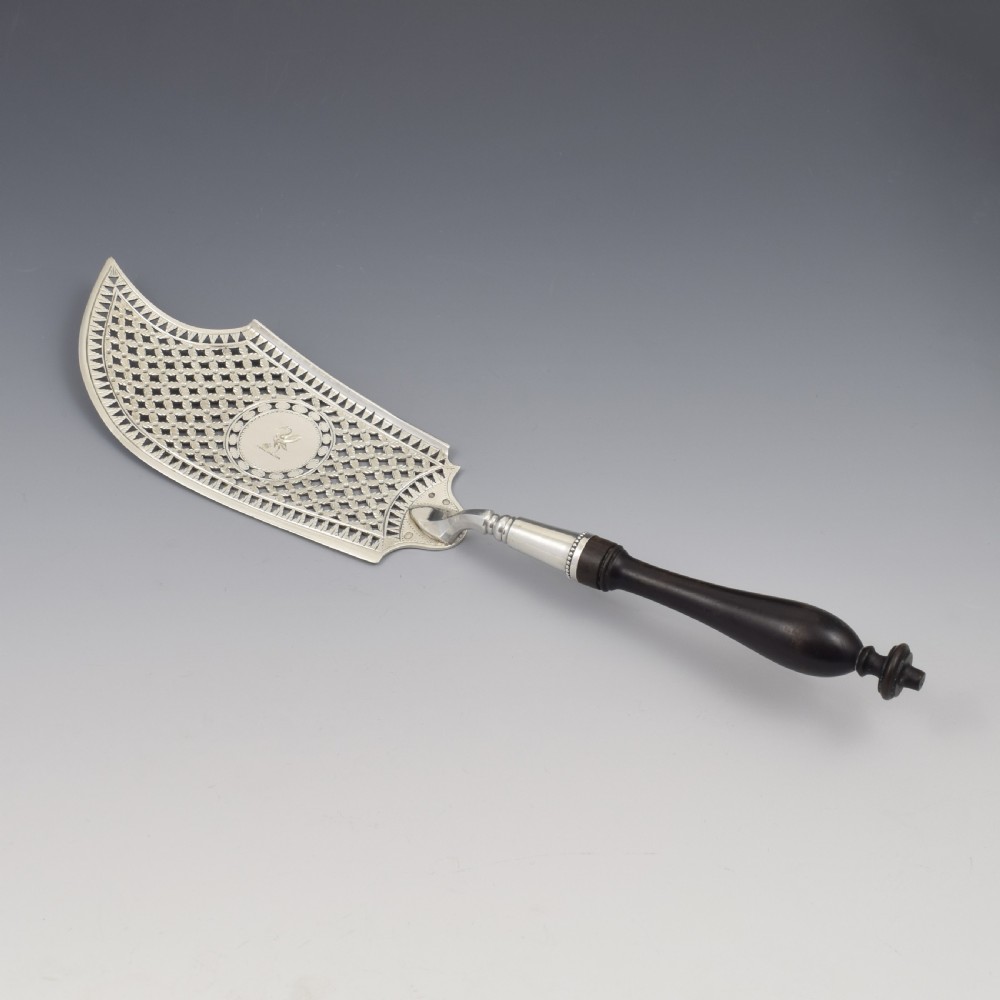 An 18th-century French silver fish slice with a pierced geometric lattice blade, an engraved crest, and a turned dark wood handle. View II