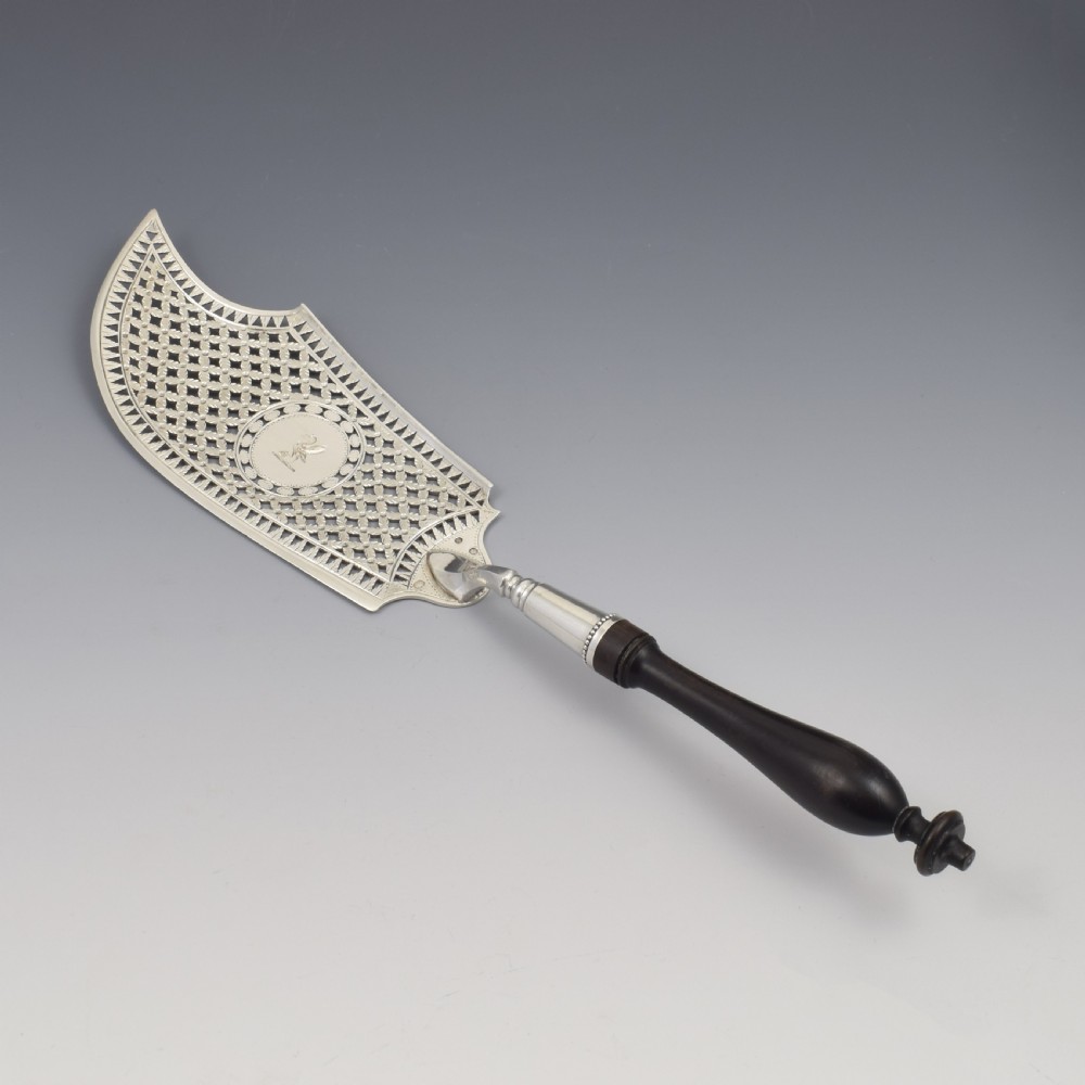 An 18th-century French silver fish slice with a pierced geometric lattice blade, an engraved crest, and a turned dark wood handle. View III