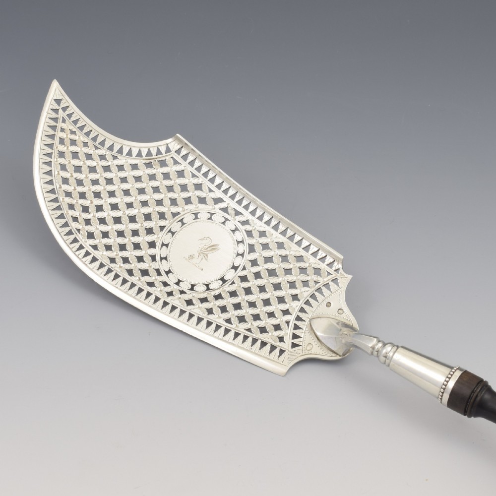An 18th-century French silver fish slice with a pierced geometric lattice blade, an engraved crest, and a turned dark wood handle. View IV