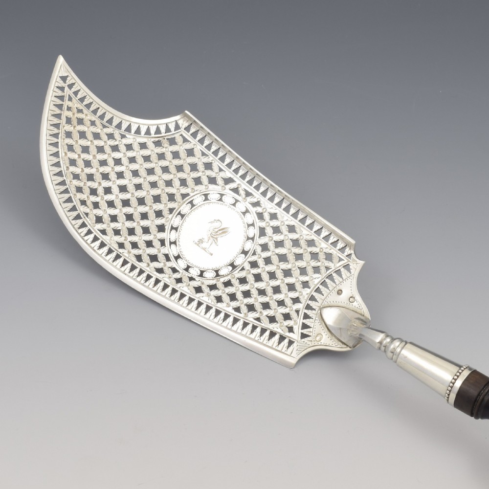 An 18th-century French silver fish slice with a pierced geometric lattice blade, an engraved crest, and a turned dark wood handle. View V