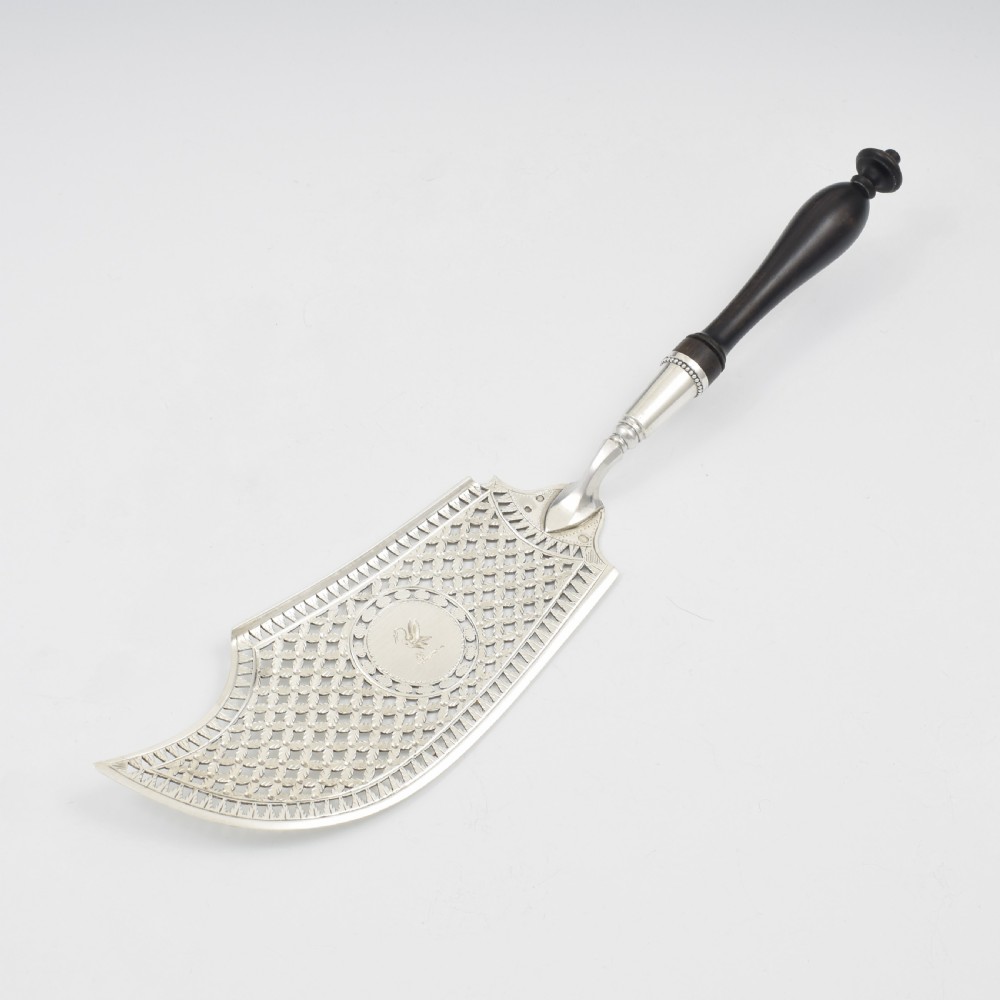An 18th-century French silver fish slice with a pierced geometric lattice blade, an engraved crest, and a turned dark wood handle. View VII