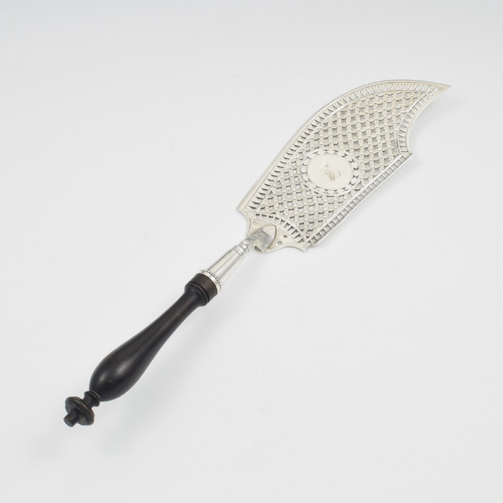 An 18th-century French silver fish slice with a pierced geometric lattice blade, an engraved crest, and a turned dark wood handle. View VIII