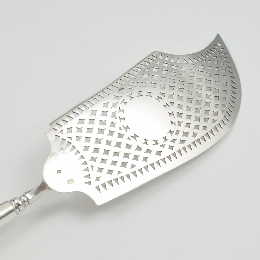 An 18th-century French silver fish slice with a pierced geometric lattice blade, an engraved crest, and a turned dark wood handle. View IX