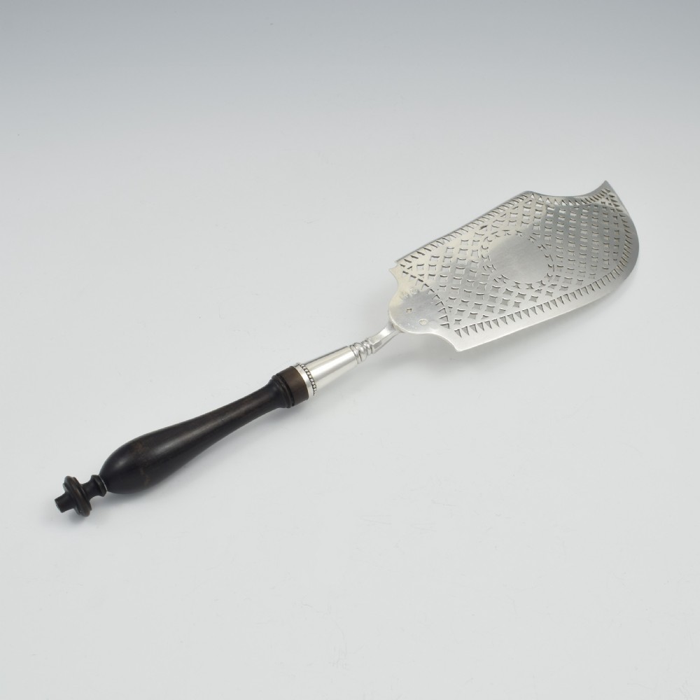 An 18th-century French silver fish slice with a pierced geometric lattice blade, an engraved crest, and a turned dark wood handle. View XI