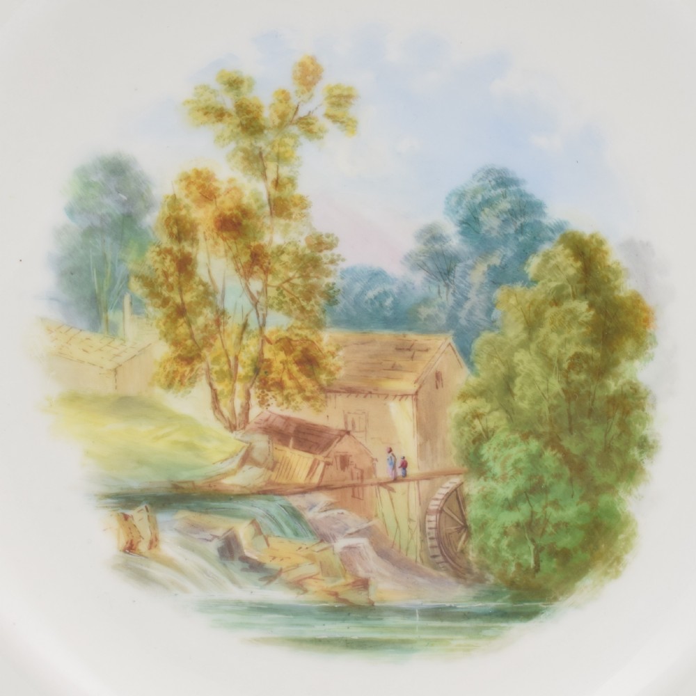 A circular porcelain cabinet plate featuring a hand-painted countryside landscape in the centre, framed by a pink ground rim with gilt and green jewelled details. View III