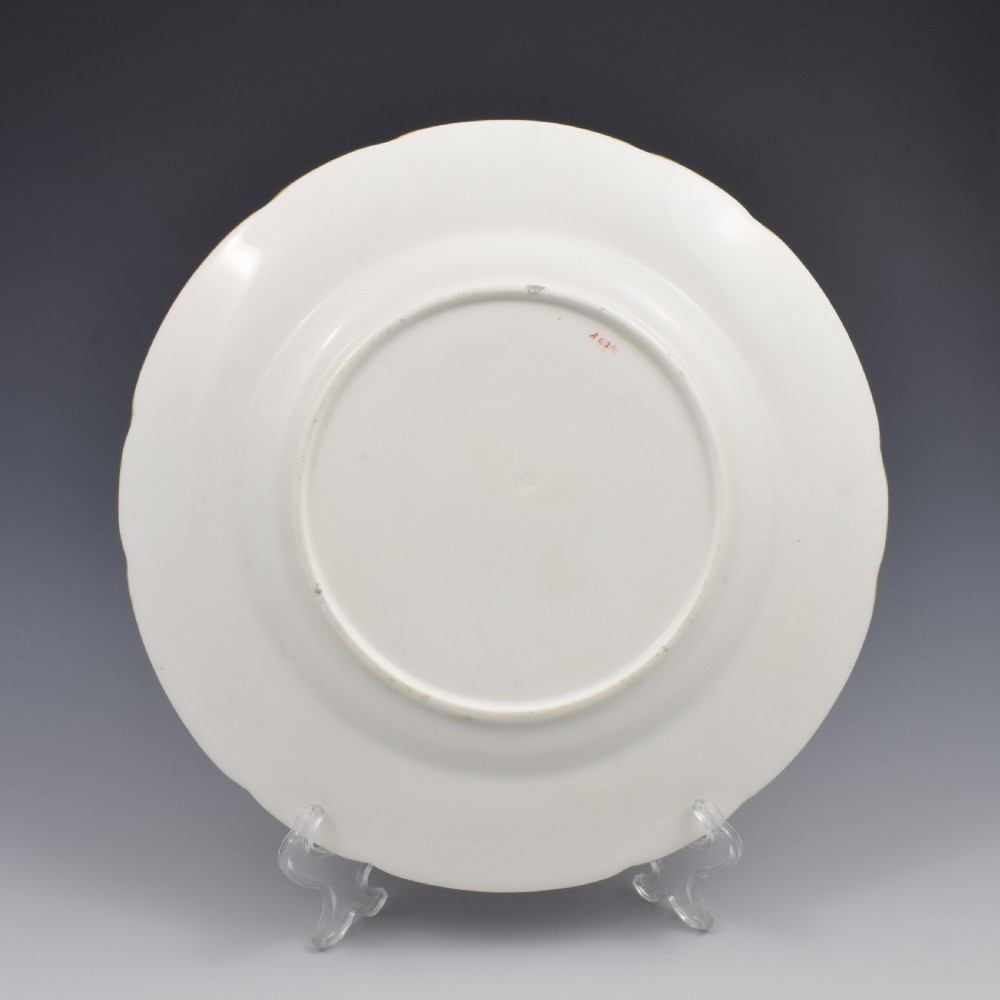 A circular porcelain cabinet plate featuring a hand-painted countryside landscape in the centre, framed by a pink ground rim with gilt and green jewelled details. View VI