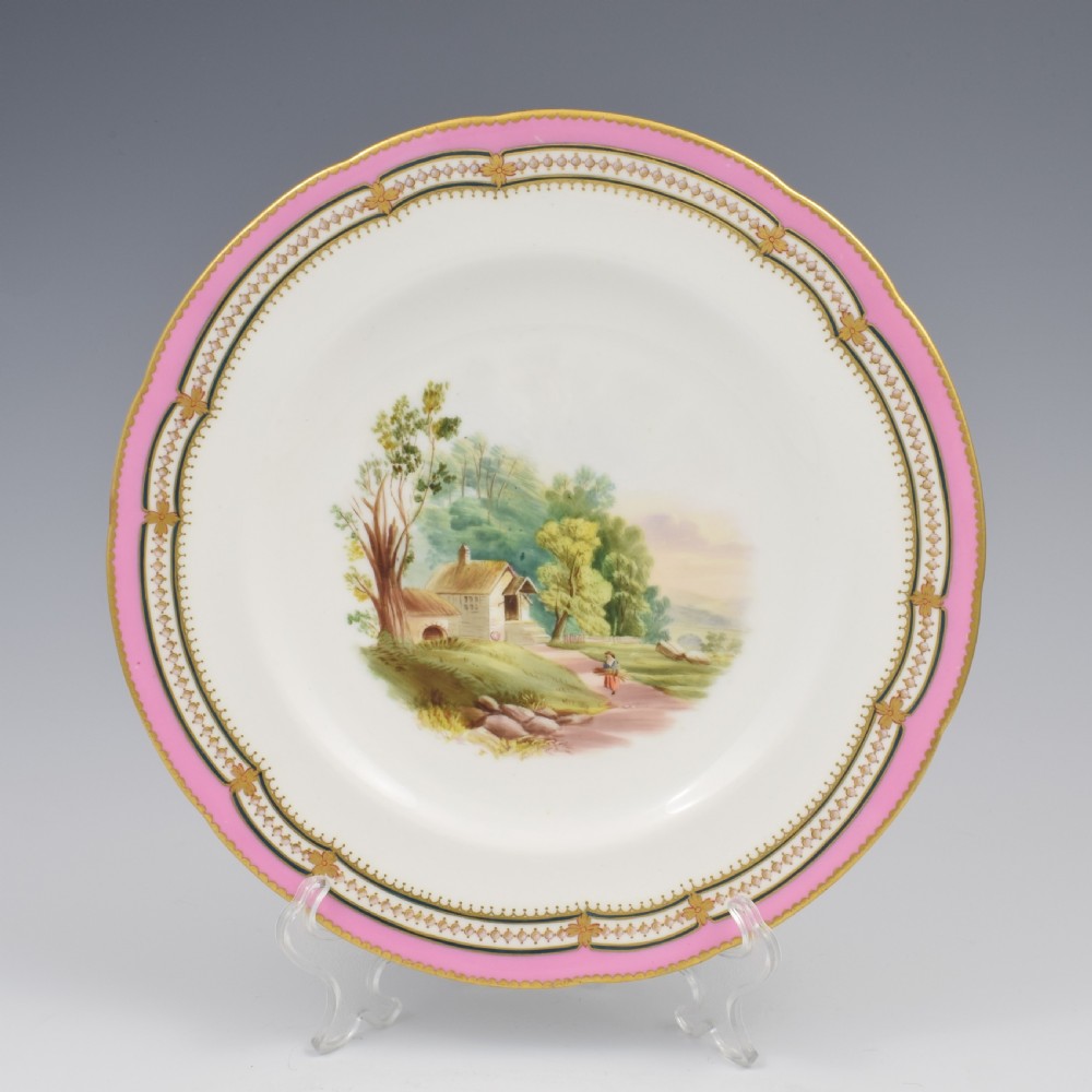 An antique porcelain dessert plate featuring a hand-painted pastoral landscape central vignette encircled by a pink border with gilded decoration and raised white enamel dots. View II