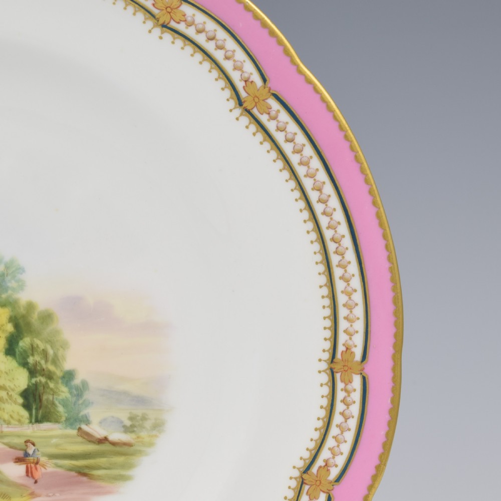 An antique porcelain dessert plate featuring a hand-painted pastoral landscape central vignette encircled by a pink border with gilded decoration and raised white enamel dots. View IV
