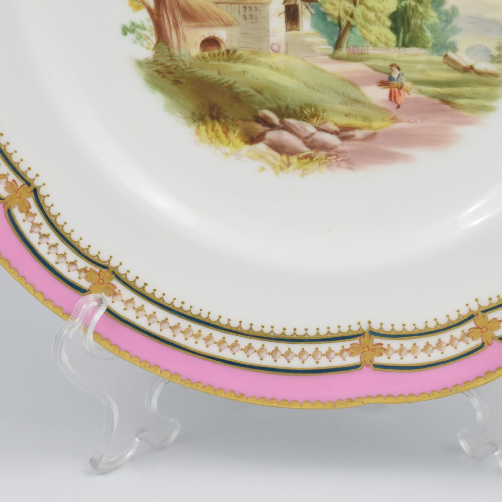 An antique porcelain dessert plate featuring a hand-painted pastoral landscape central vignette encircled by a pink border with gilded decoration and raised white enamel dots. View V
