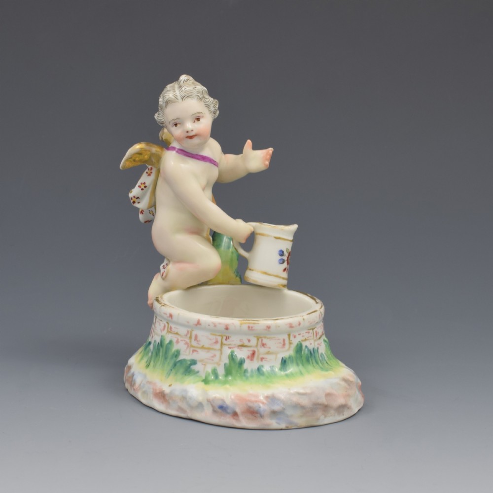 A 19th-century KPM Berlin porcelain table salt featuring a cupid figure standing beside a brick-patterned well basin with hand-painted details. View II