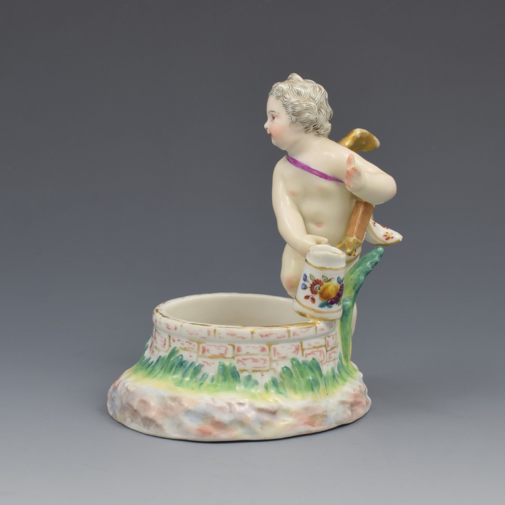 A 19th-century KPM Berlin porcelain table salt featuring a cupid figure standing beside a brick-patterned well basin with hand-painted details. View IV