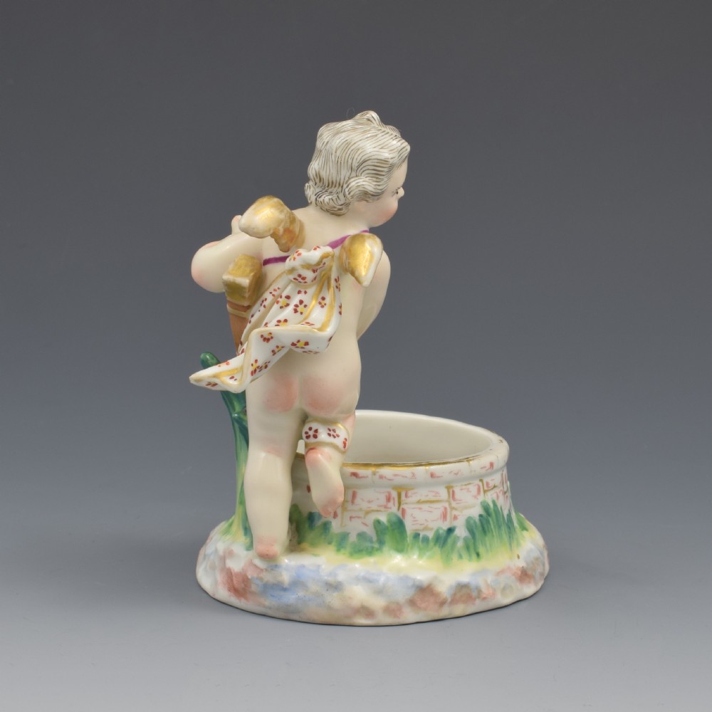 A 19th-century KPM Berlin porcelain table salt featuring a cupid figure standing beside a brick-patterned well basin with hand-painted details. View VII