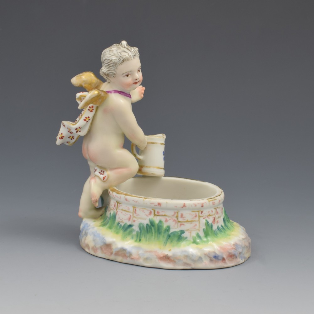 A 19th-century KPM Berlin porcelain table salt featuring a cupid figure standing beside a brick-patterned well basin with hand-painted details. View VIII