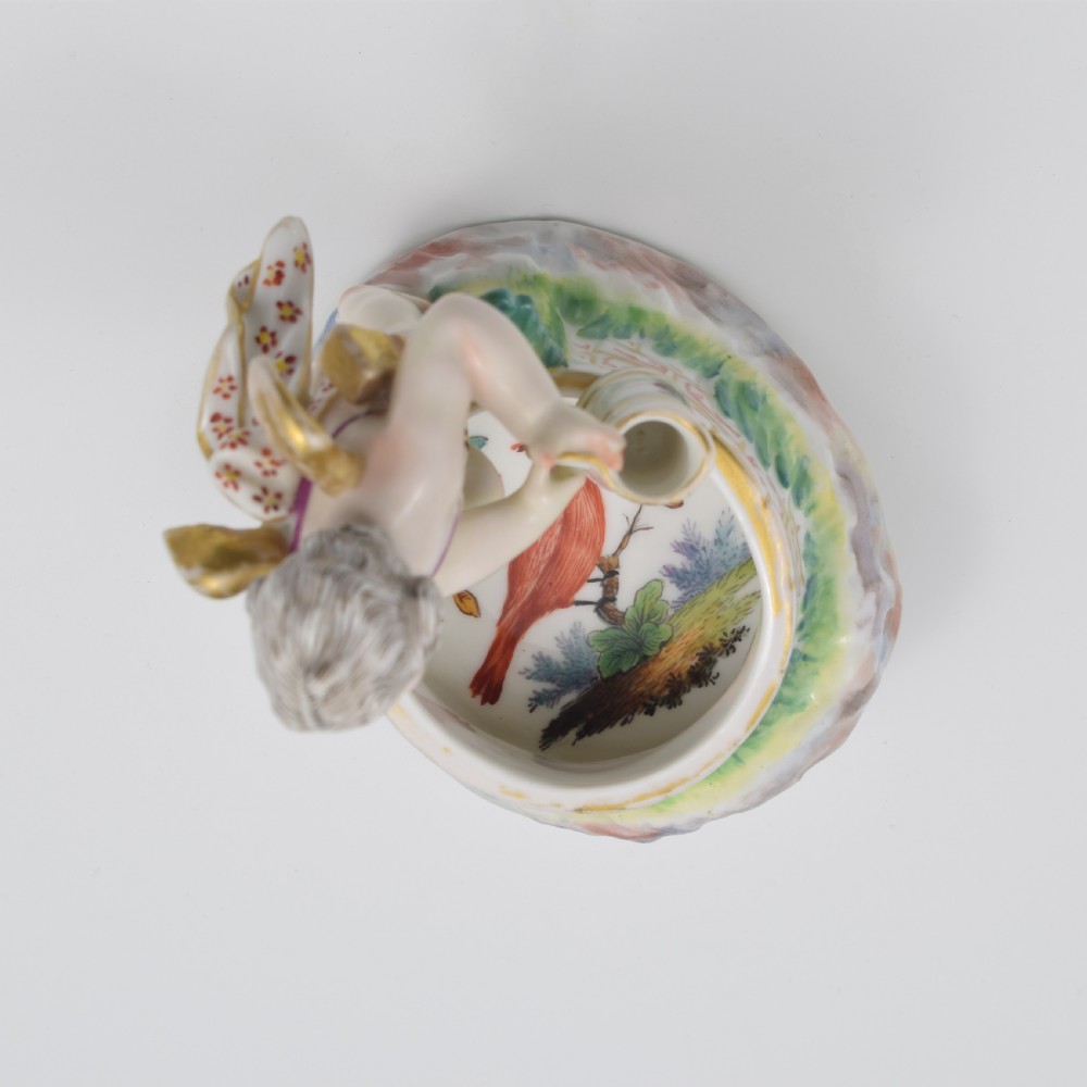 A 19th-century KPM Berlin porcelain table salt featuring a cupid figure standing beside a brick-patterned well basin with hand-painted details. View X