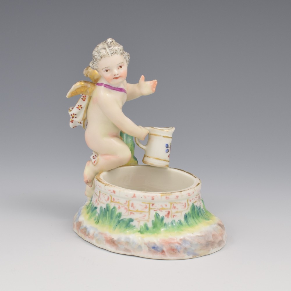 A 19th-century KPM Berlin porcelain table salt featuring a cupid figure standing beside a brick-patterned well basin with hand-painted details. View XIV