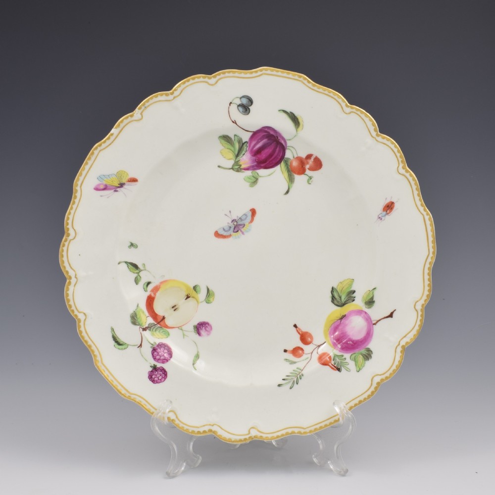 An eighteenth-century soft-paste porcelain dessert plate with a lobed gilded rim, decorated with hand-painted fruit motifs and insects against a white background.