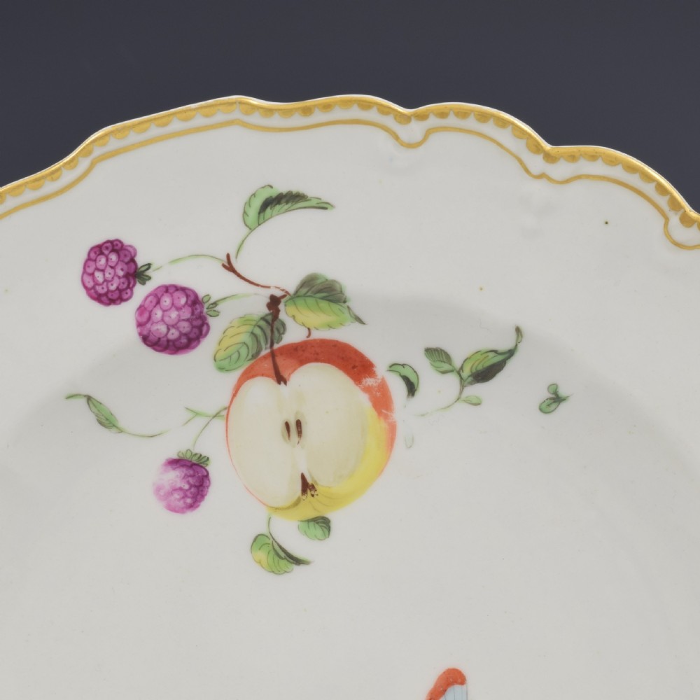 An eighteenth-century soft-paste porcelain dessert plate with a lobed gilded rim, decorated with hand-painted fruit motifs and insects against a white background. View IV
