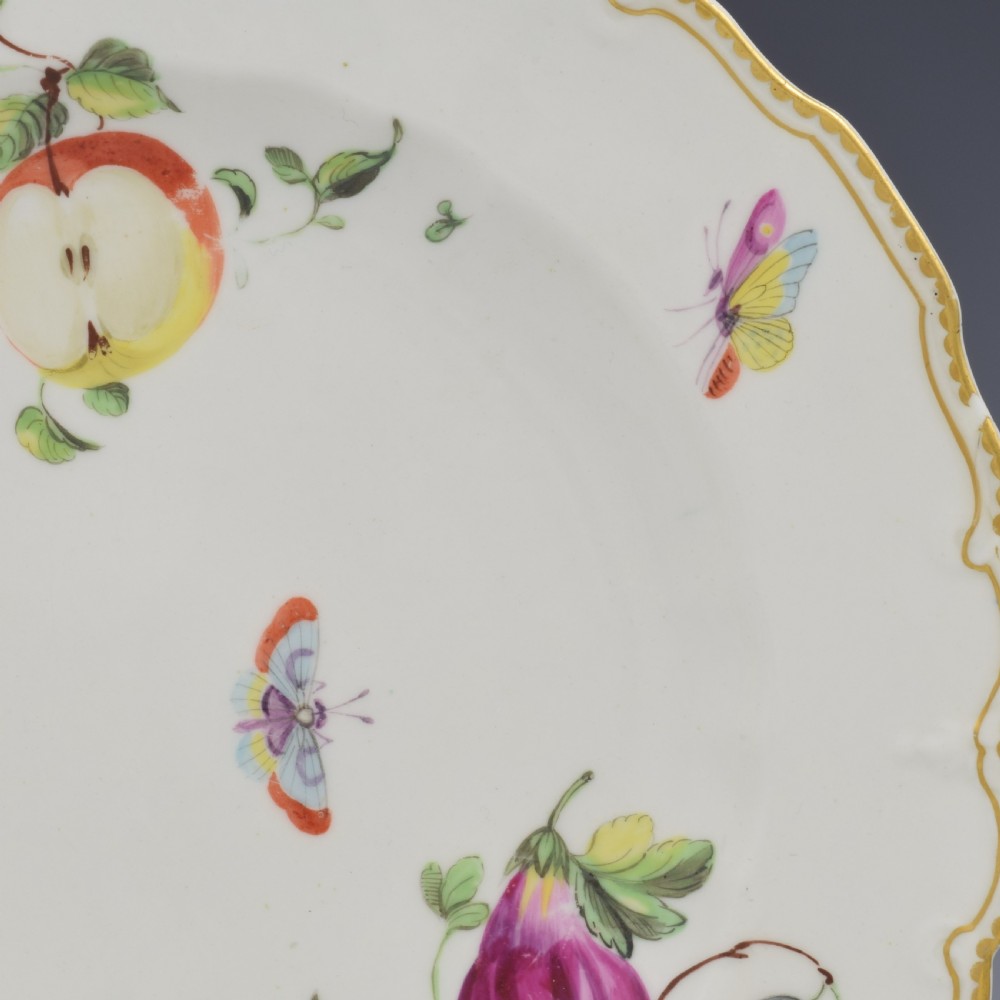 An eighteenth-century soft-paste porcelain dessert plate with a lobed gilded rim, decorated with hand-painted fruit motifs and insects against a white background. View V