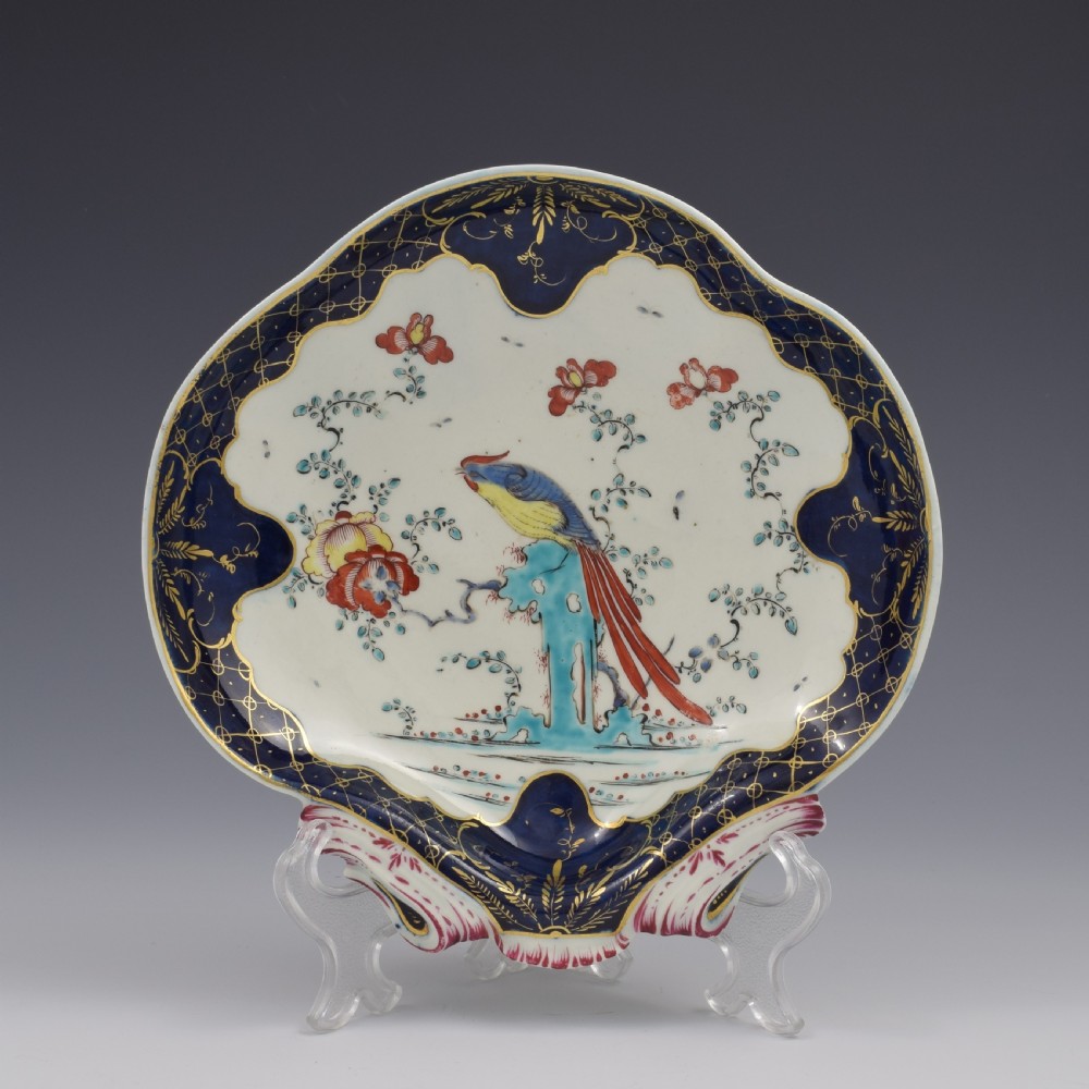 An eighteenth-century shell-shaped soft-paste porcelain dessert dish featuring a hand-painted exotic bird, floral motifs, and a cobalt blue border detailed with gilded lattice work.