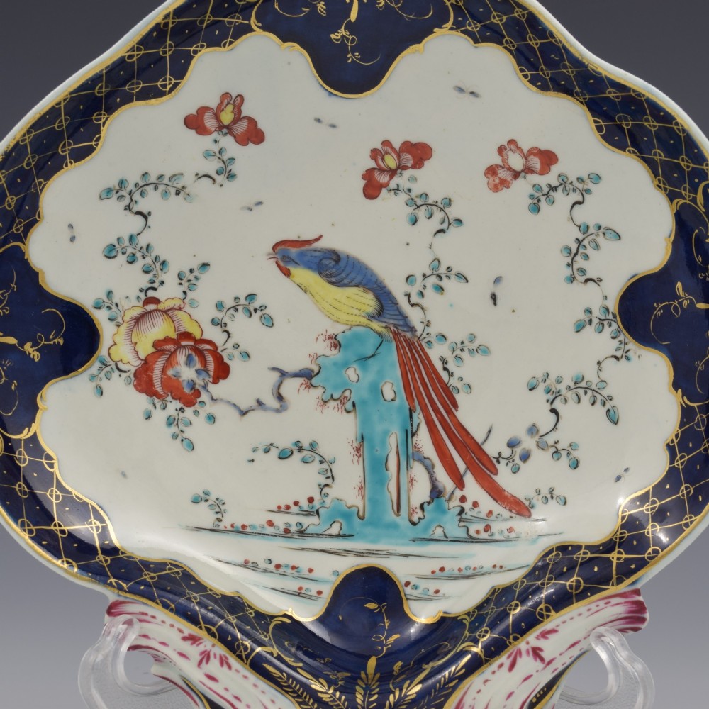 An eighteenth-century shell-shaped soft-paste porcelain dessert dish featuring a hand-painted exotic bird, floral motifs, and a cobalt blue border detailed with gilded lattice work. View II