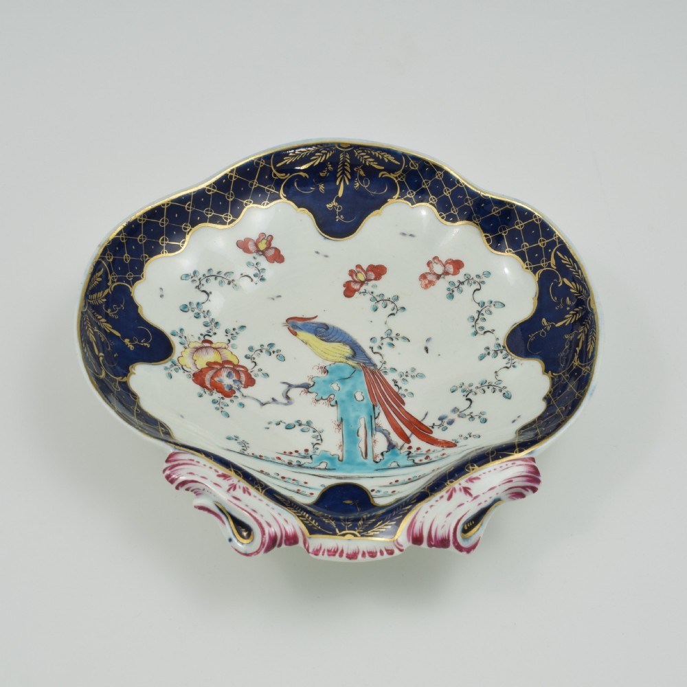 An eighteenth-century shell-shaped soft-paste porcelain dessert dish featuring a hand-painted exotic bird, floral motifs, and a cobalt blue border detailed with gilded lattice work. View V