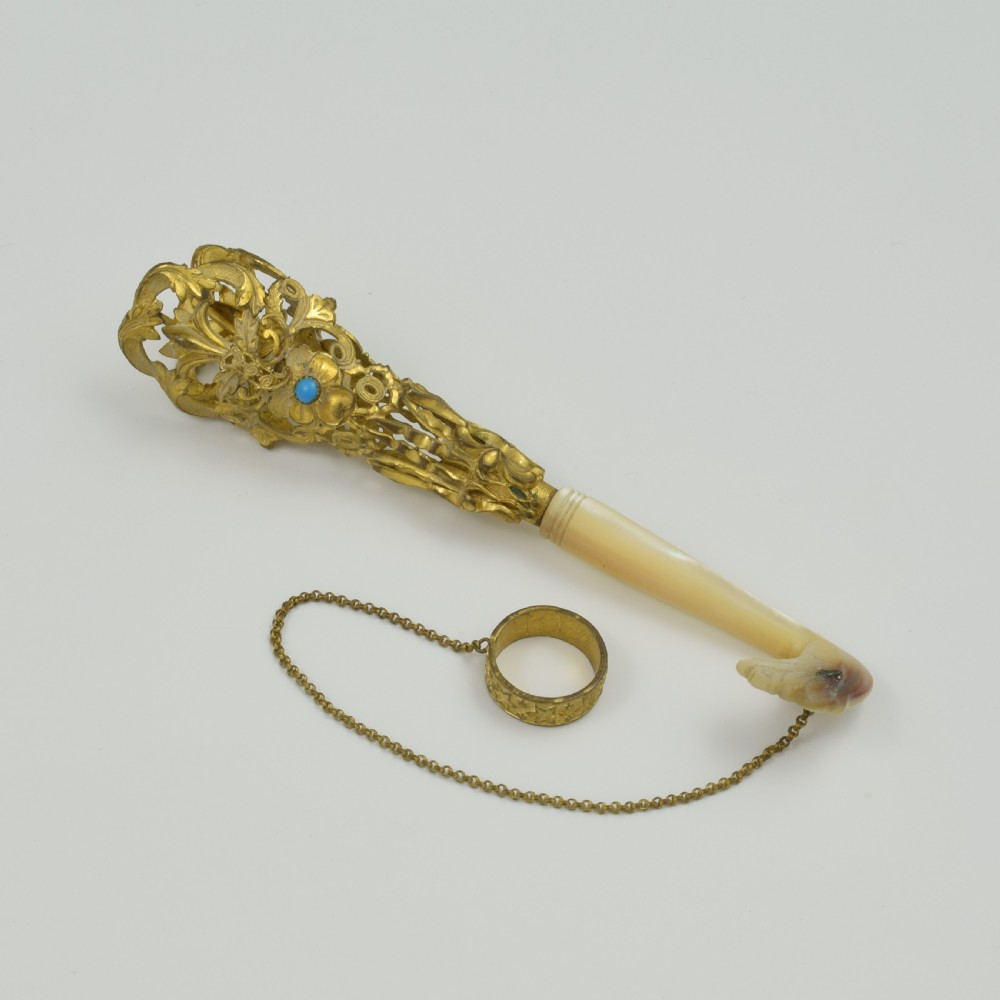 An antique French gilt ormolu tussie mussie posy holder featuring elaborate pierced metalwork set with a turquoise stone, a carved mother-of-pearl handle, and a finger ring attached by a chain.